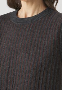 Mørkegrå strikket sweater med ribbet tekstur, der har tynde brune striber. Designet inkluderer en rund halsudskæring og en blød, behagelig fornemmelse.