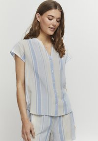 Blusa leggera a maniche corte in crema con strisce verticali blu e beige. Presenta un collo a V e dettagli con bottoni sul davanti.