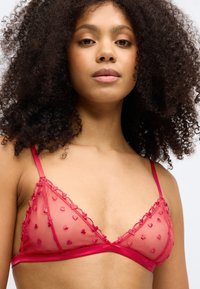 Κόκκινο διάφανο τρίγωνο σουτιέν με κεντημένα σχέδια καρδιάς, οδοντωτό τελείωμα και ρυθμιζόμενες τιράντες. Λείο κάτω μέρος για υποστήριξη.