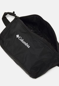 Pungă neagră din nylon cu închidere cu fermoar și curea ajustabilă. Prezintă logo-ul Columbia în alb pe față, textură netedă și formă rectangulară.