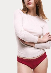 Ljust grå långärmad tröja i kombination med röda trosor med spetsdetaljer, som visar upp en figurnära design och mjuk textur.