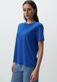 Niebieska koszulka z okrągłym dekoltem, wykonana z miękkiego materiału, z krótkimi rękawami, o luźnym kroju, zestawiona z jasnoniebieskimi dżinsami. Gładka tekstura, minimalistyczny design.