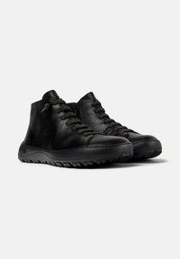 Zwarte leren high-top casual schoenen met vetersluiting en gestructureerde rubberen zolen op een witte achtergrond.