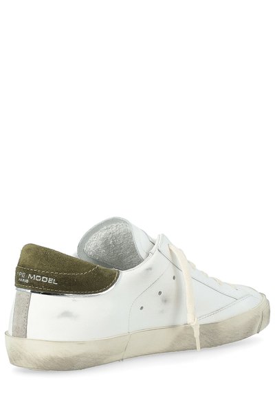 Zapatilla blanca de estilo retro con una lengüeta en el talón de ante verde texturizado. Presenta acentos metálicos, cordones planos y una suela de goma desgastada.