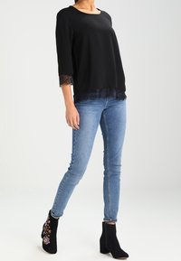 Top nero con bordo in pizzo, maniche a tre quarti, abbinato a jeans skinny blu e stivaletti neri con ricami floreali.