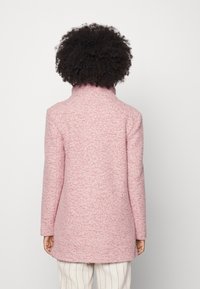 Růžový kabát z vlněné směsi s texturovaným povrchem, vysokým límcem a dlouhými rukávy, s rovný střihem a délkou do poloviny stehna.