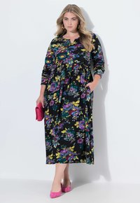 Černé květinové šaty s dlouhými rukávy, zdobené živými fialovými a žlutými květinami. Šaty mají volný střih a boční kapsy.