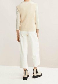 Beige ribbad stickad väst över en vit långärmad topp, kombinerad med vida vita byxor och chunky kängor med svarta detaljer.