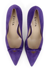 Scarpe col tacco alto in suede viola con punta affusolata, caratterizzate da lati intagliati e un'accaanto a fiocco sul davanti, l'etichetta interna riporta "EVITA."