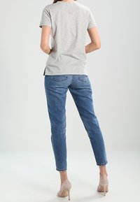 T-shirt grigia a maniche corte con una vestibilità comoda, abbinata a jeans di denim blu. I jeans presentano un taglio dritto e dettagli di cuciture sottili.