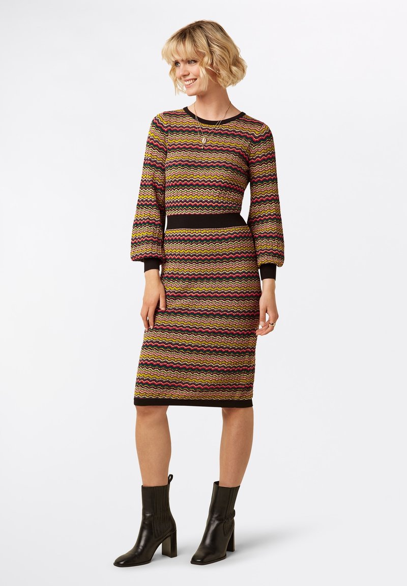 Abito a fantasia con un design ondulato in marrone, rosa, giallo e nero. Maniche lunghe, silhouette aderente e taglio al ginocchio. Stivali neri.