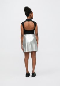 Zwarte mouwloze top met een uitsnijding aan de achterkant, gecombineerd met een glanzende zilveren minirok. Zwarte schoenen maken de outfit compleet. Eenvoudig en modern design.