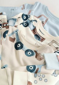 Vier Sweatshirts übereinander gestapelt; sie zeigen hellblaue, cremefarbene und beige Stoffe mit verspielten grafischen Mustern von Fahrzeugen und Werkzeugen. Rippbündchen an Ärmeln und Kragen.