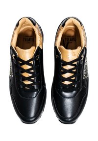 Zapatillas sintéticas negras con acentos dorados, que presentan una textura suave, seis ojales y un interior marrón claro con detalles impresos sutiles.