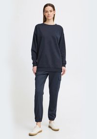 Mørkeblå sweatshirt med en afslappet pasform, rund halsudskæring og lange ærmer, parret med matchende tapered cargo-bukser og lyse sneakers.