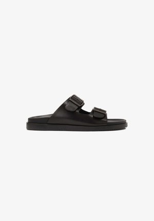 Black leather sandals featuring two adjustable buckled straps, flat sole, and minimalistic design with a smooth texture.
