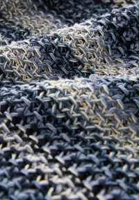 Tissu texturé dans des nuances de bleu et de crème, avec un motif tissé créant de la profondeur et de la variation, présentant des fibres lâches et douces.