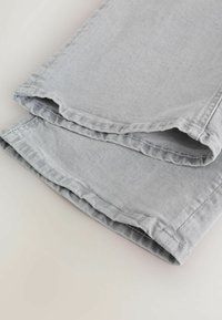 Jean en denim gris clair, plié au niveau de l'ourlet inférieur, montrant les coutures et la texture du tissu sur une surface neutre.