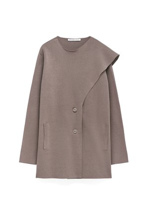 Veste taupe à manches longues avec un rabat asymétrique sur le devant, deux boutons et deux poches à fente verticales, fabriquée en tissu lisse.
