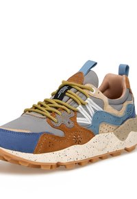 Športni športni copat z mešanimi materiali—sivega zgornjega dela z modrimi, rjavimi in kremnimi poudarki. Rumene vezalke in pegasta podplat. Teksturiran zaključek.