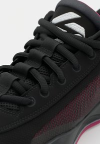Schwarze Sportschuhe aus Mesh- und Gummimaterialien, mit schwarzen Schnürsenkeln, einer strukturierten Seitenpartie mit lila Akzenten und einer gepolsterten Zunge.