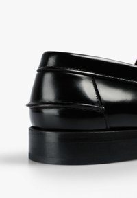 Zapato de cuero negro con un diseño elegante, tacón redondeado, detalles de costura sutiles y un acabado brillante y suave sobre una suela negra sólida.