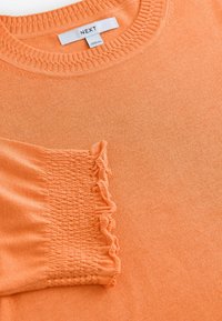 Maglione arancione con scollatura a girocollo a coste e un dettaglio testurizzato e arricciato sulla manica. Realizzato in un tessuto morbido; finitura liscia.