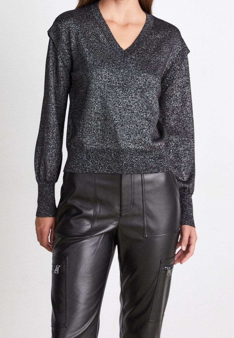 Schwarzer, glitzernder V-Ausschnitt-Pullover mit langen Ärmeln und gerippten Bündchen, kombiniert mit hoch taillierten schwarzen Lederhosen mit Reißverschlusstaschen.