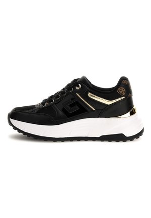 Sneaker nera con suola spessa bianca, dettagli dorati, tallone a fantasia marrone e lacci neri, vista di lato.