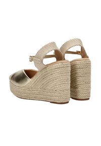 Sandalias de cuña espadrille con una puntera metálica dorada, correas tejidas en color beige y un tacón de yute texturizado con un patrón ondulado.