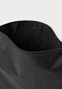 Crna torba s glatkom, mat površinom. Ima unutarnji džep sa zatvaračem i mekan, fleksibilan materijal.Jednostavan, funkcionalan dizajn.
