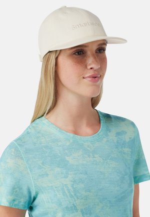 Lys beige kasket med et broderet logo, struktureret design, buet skygge, båret med en blå mønstret T-shirt. Glat stofoverflade.