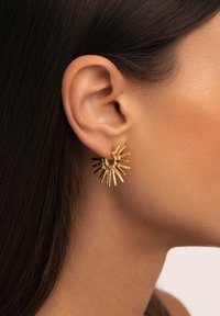 Orecchini color oro con design a raggi di sole, caratterizzati da punte appuntite e testurizzate e una combinazione di finiture opache e lucide.