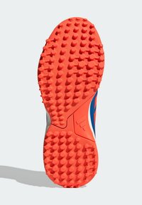 Semelle d'une chaussure de sport orange avec de nombreux crampons arrondis pour une meilleure adhérence, montrant une partie de la tige bleue et blanche.