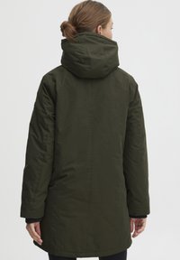 Manteau long vert olive avec capuche, présentant une texture lisse et mate ainsi qu'un design minimaliste. Comprend des poignets et une coupe droite.