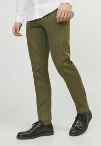 Olive green cotton chinos with a slim fit, featuring a smooth texture and side pockets, paired with black leather shoes.