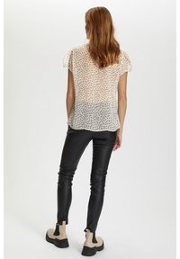 Blouse transparente à manches courtes avec un motif à pois en crème et marron. Associée à un pantalon slim noir et des bottines beiges.