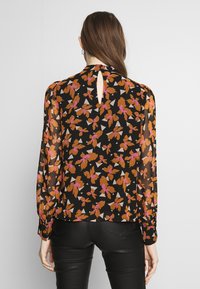 Svart transparent blus med blommönster i orange, rosa och beige; har långa ärmar och detalj med nyckelhål bak.