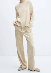 Pull beige en maille avec encolure ronde et ourlet côtelé, associé à un pantalon beige à jambes larges en tissu doux. Design simple.