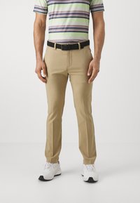 Pantalones beige hechos de una tela suave, con un corte ajustado. Combinados con una camisa polo a rayas y un cinturón negro texturizado. Zapatillas blancas.