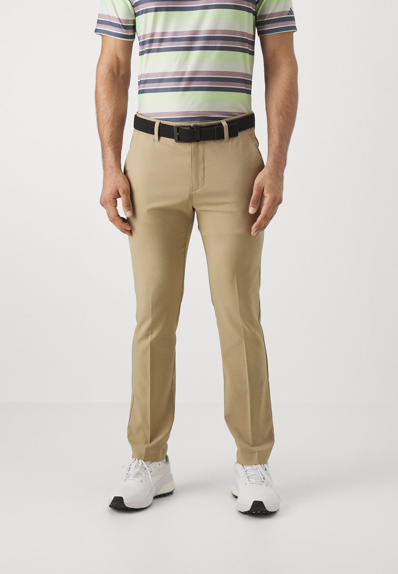 Pantalones beige hechos de una tela suave, con un corte ajustado. Combinados con una camisa polo a rayas y un cinturón negro texturizado. Zapatillas blancas.
