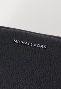 Zwarte leren portemonnee met een textuur op het oppervlak en een metallic zilveren "MICHAEL KORS" logo aan de voorkant.
