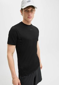 Schwarzes sportliches T-Shirt mit figurbetontem Schnitt, kurzen Ärmeln und glatter Textur. Mit kleinem Logo im Brustbereich.