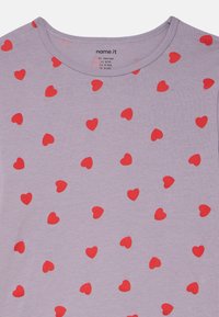 Ανοιχτό μωβ βαμβακερό T-shirt με στρογγυλή λαιμόκοψη, διακοσμημένο με διασκορπισμένα κόκκινα σχέδια καρδιών σε όλο το ύφασμα. Απαλή υφή, casual σχεδιασμός.