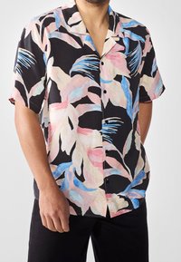 Short-sleeved shirt in black fabric featuring a colorful tropical leaf pattern in pink and blue. Five buttons down the front with a collar.