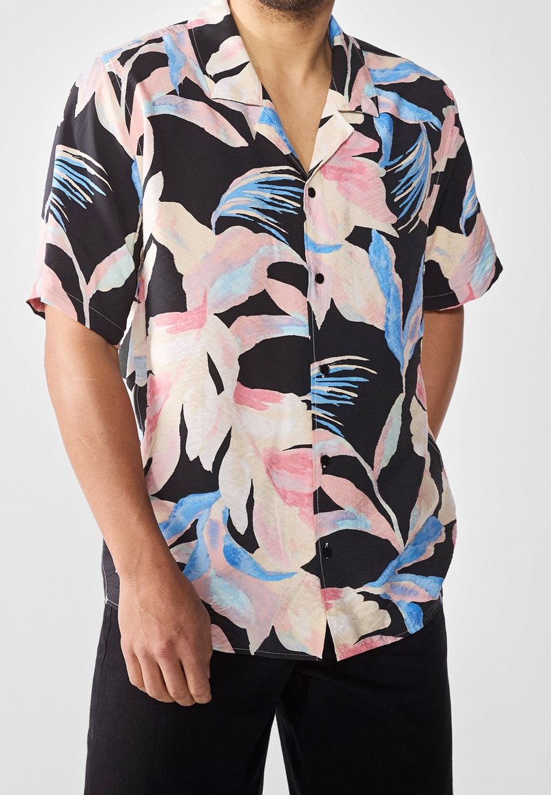 Short-sleeved shirt in black fabric featuring a colorful tropical leaf pattern in pink and blue. Five buttons down the front with a collar.