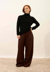 Czarny prążkowany sweter z golfem zestawiony z luźnymi, ciemnobrązowymi spodniami. Stylizacja cechuje się gładką teksturą i swobodnym krojem.