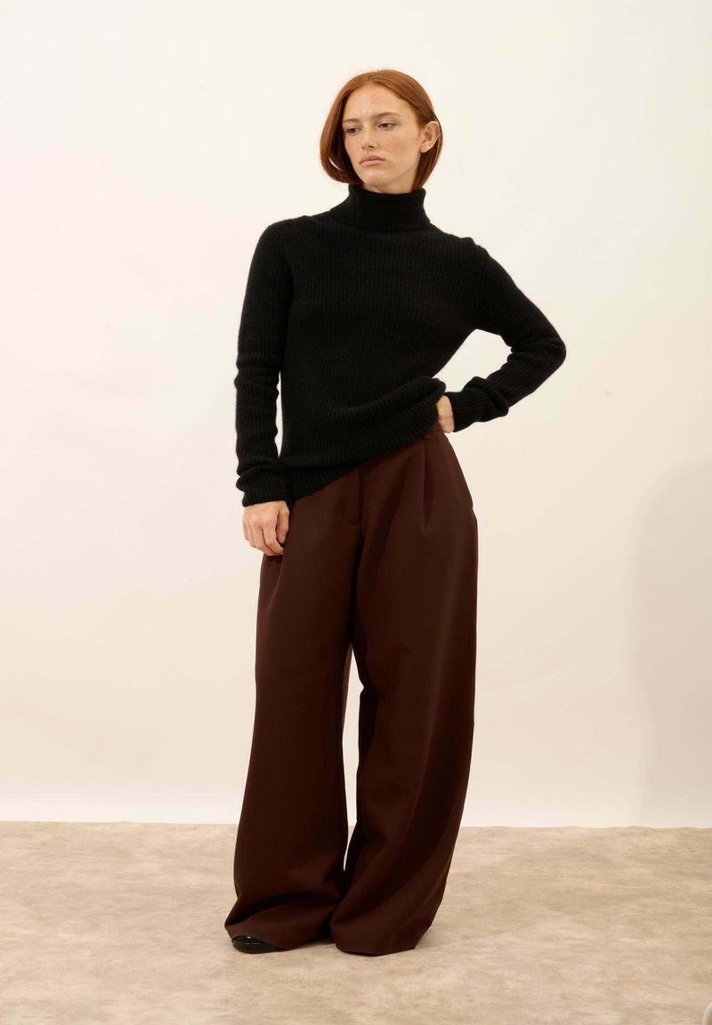 Czarny prążkowany sweter z golfem zestawiony z luźnymi, ciemnobrązowymi spodniami. Stylizacja cechuje się gładką teksturą i swobodnym krojem.