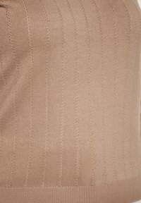 Beige gerippter Strickoberteil mit vertikalen Streifen, glatter Textur und einer taillierten Passform, bei der der Saum flach anliegt.