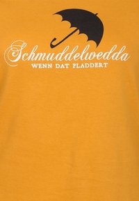Gul bomullströja med en svart paraplygrafik och vit text som säger "Schmuddelwedda WENN DAT PLADDERT." Slät yta.